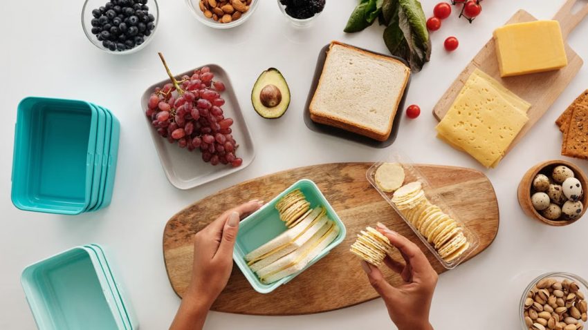 Top view of preparing a healthy lunch with fruits, cheese, and crackers, showcasing fresh ingredients and a vibrant lifestyle.