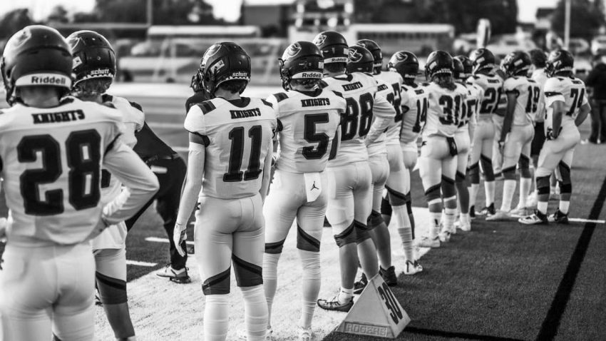 Black and white photo of a high school football team lining up on the field pre-game.